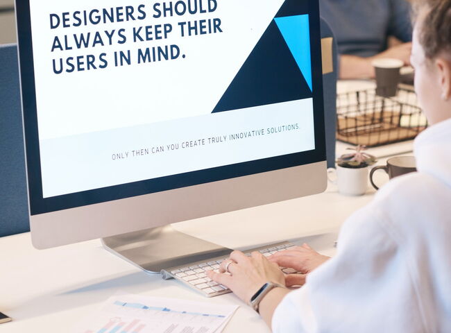 UX Designerin vor einem Monitor mit der Aufschrift "Designers schould always keep their users in mind.".