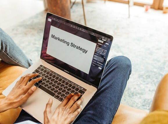 Eine Person auf einem Sofa hat einen Laptop auf dem Schoß. Auf diesem ist ein Dokument mit dem Titel Marketing Strategy geöffnet.