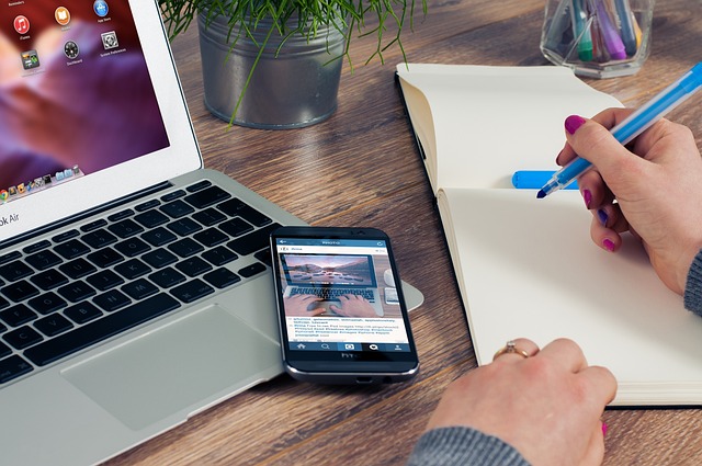 Eine Frau macht sich Notizen zu ihrer Social Media Strategie auf einem Block. Neben ihr steht ein Laptop und ein Smartphone.